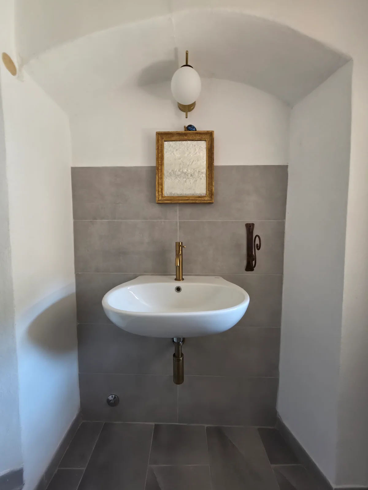 Il lavabo bianco della toilette al piano terra, con rubinetto dorato e specchio sotto la volta